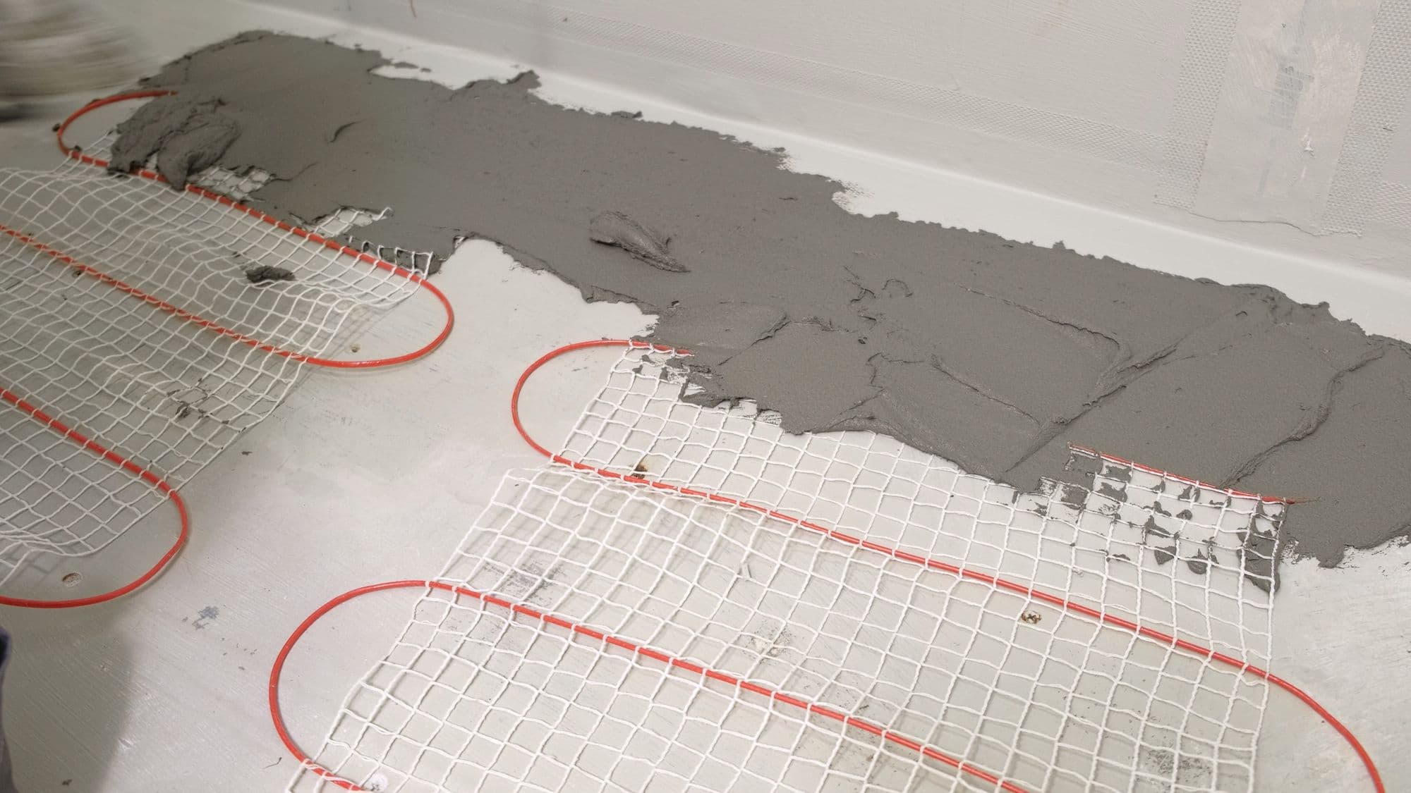 An electric underfloor heating mat being bedded in tile adhesive